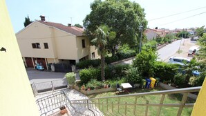 Zona residencial con un edificio amarillo, una escalera que lleva a un balcón y un jardín con diversas plantas y una palmera.