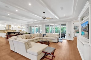A spacious living room with a large L-shaped sectional sofa, a ceiling fan, and a dining area with a kitchen in the background. - Luxe Modern Design 5000sf/Heated pool/Gameroom (Hollywood)