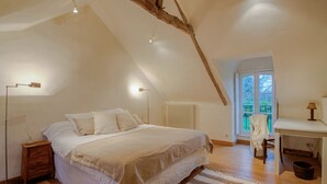 Ein Schlafzimmer mit schrägem Dach, einem großen Bett, Nachttischlampen, einem Heizkörper, einem Schreibtisch und einem Sessel.