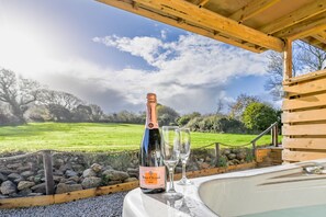 A bottle of champagne and two glasses on a table with a view of a grassy field and trees. - Morley's (Truro)
