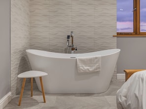 Ein modernes Badezimmer mit einer freistehenden Badewanne, einem kleinen runden Tisch und einem Fenster mit Blick zum Himmel.