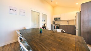 Een moderne keuken met witte kasten, een magnetron en een koelkast. Er staat een eettafel met stoelen en er hangt een plafondventilator.
