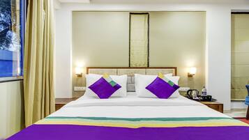 A hotel room with a large bed, two bedside tables, a nightstand, a window with curtains, and a view of trees outside.