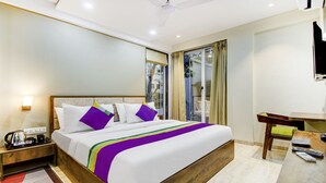Ein Hotelzimmer mit einem großen Bett, einem Nachttisch mit Wasserkocher, einem Schreibtisch mit Stuhl und einem an der Wand befestigten Fernseher.