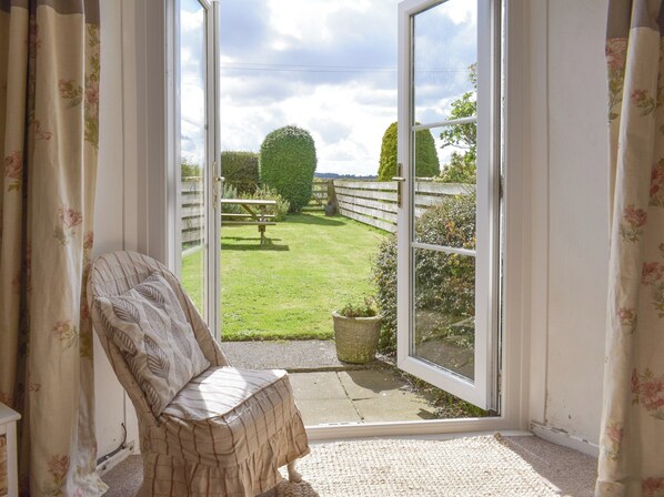 A room with a view of a grassy yard, a wooden fence, and a picnic table.