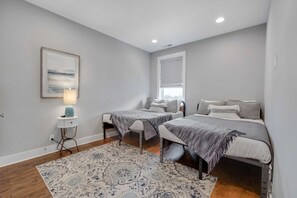 Un dormitorio con dos camas, una mesita de noche, una lámpara y una ventana.