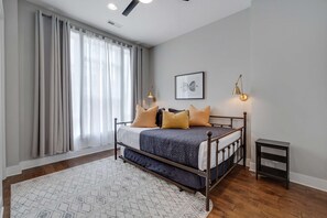 A bedroom with a bed, a bedside table, a lamp, and a window with curtains. - Stunning Downtown Nashville Home with City Views (Nashville)