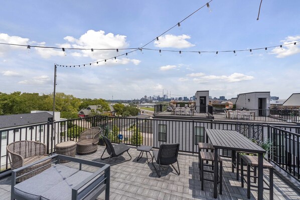 A rooftop terrace with wicker furniture, a table, and string lights.