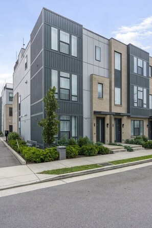A modern multi-story residential building with a grey facade, large windows, and a small front garden with a tree and shrubs. - Stunning Downtown Nashville Home with City Views (Nashville)