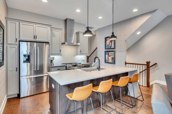 Een moderne keuken met een centraal eiland, roestvrijstalen apparatuur en een backsplash met een herringbone-patroon.