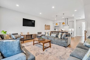 A modern living room with a grey sofa, a wooden coffee table, and a flat-screen TV mounted on the wall.