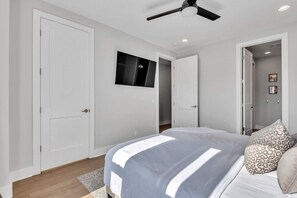 A bedroom with a bed, a ceiling fan, a TV, and a wardrobe.