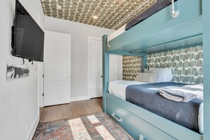 Ein Schlafzimmer mit einem Bett, einem an der Wand montierten Fernseher, einem gemusterten Teppich und einer Tür.