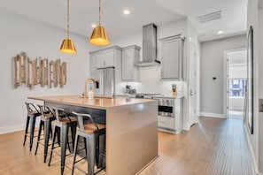 A modern kitchen with a central island, bar stools, stainless steel appliances, and pendant lighting.