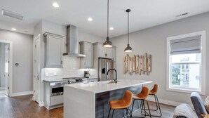 A modern kitchen with a central island, stainless steel appliances, and pendant lighting. - Two Luxe Nashville Homes + Downtown Skyline Views (Nashville)
