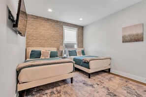 A bedroom with two beds, a window, a mounted TV, and a painting on the wall. - 2 Massive Nashville Homes - Stunning Downtown View (Nashville)