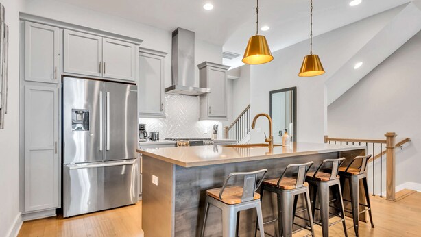 A modern kitchen with stainless steel appliances, a central island with bar stools, and pendant lighting. - Two Luxe Nashville Homes + Downtown Skyline Views (Nashville)