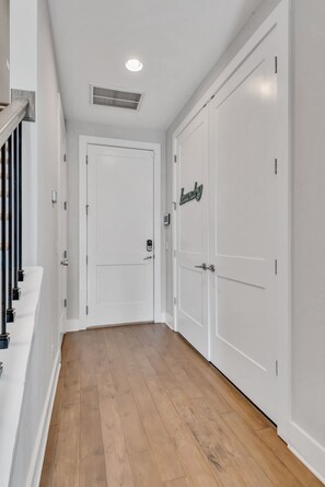 A hallway with white doors, a wooden floor, and a ceiling vent.