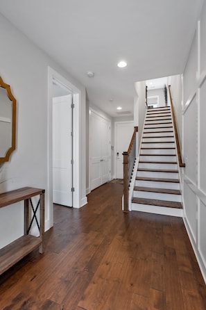 A hallway with wooden flooring, white walls, and a wooden staircase with a handrail.