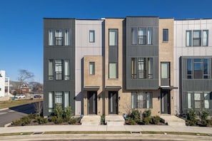 A modern multi-story residential building with a symmetrical facade, large windows, and a flat roof.