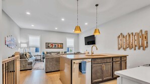 A modern kitchen with a central island, pendant lighting, and a dining area with a sofa and a TV. - Two Luxe Nashville Homes + Downtown Skyline Views (Nashville)