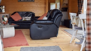 A cozy living room with a black leather sofa, a black reclining chair, and a wooden dining table with white chairs. - Pheasant Lodge - UK33402 (Billesdon, near Leicester)