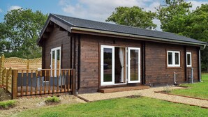 A wooden cabin with a sloped roof, large sliding glass doors, and a fenced deck area. - Pheasant Lodge - UK33402 (Billesdon, near Leicester)