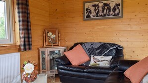 A cozy cabin interior with a black leather sofa, a glass coffee table, and a wooden cabinet with glass doors. - Pheasant Lodge - UK33402 (Billesdon, near Leicester)