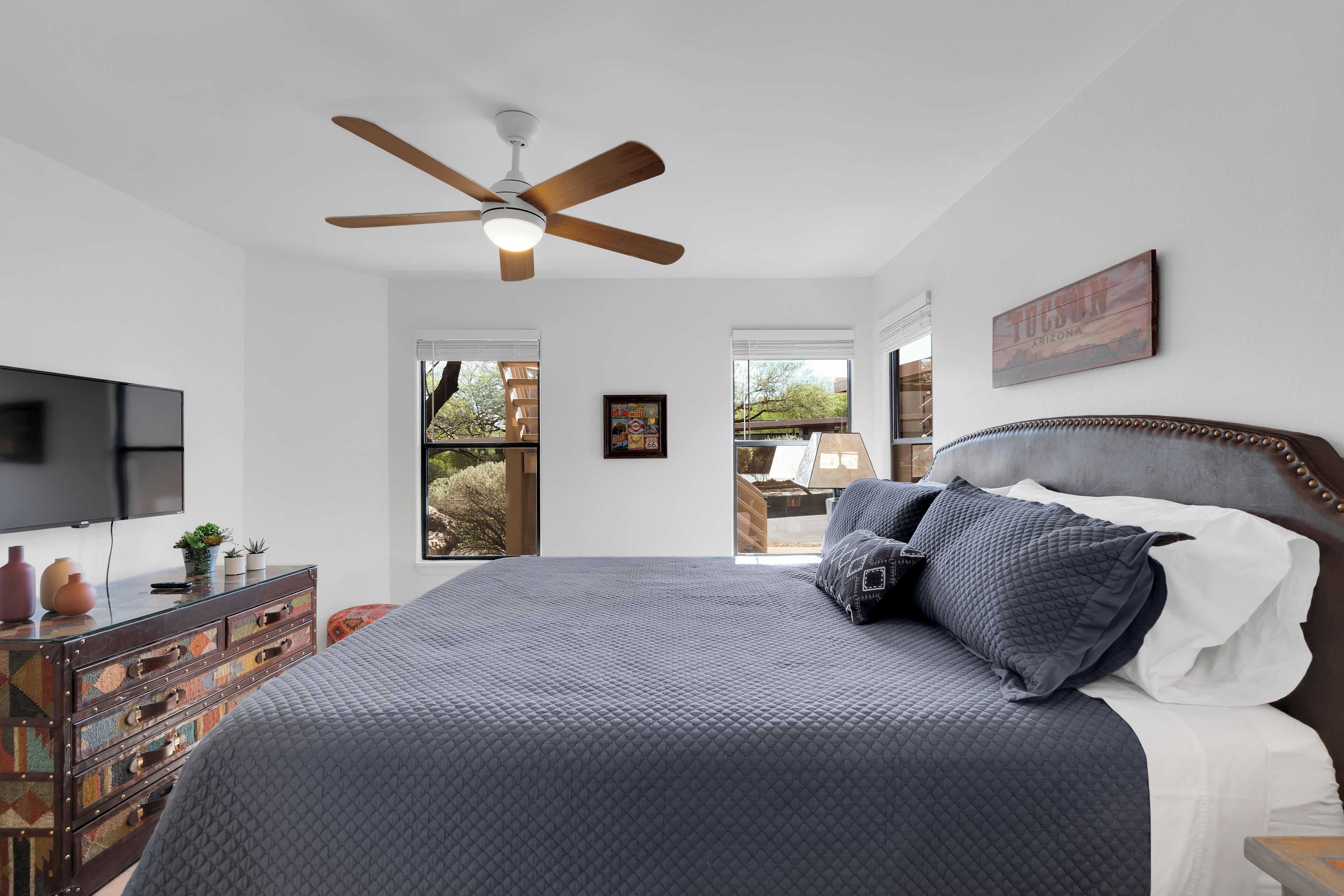 A bedroom with a large bed, a ceiling fan, a TV, and a dresser with drawers.