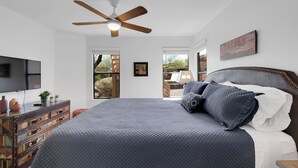 A bedroom with a large bed, a ceiling fan, a TV, and a dresser with drawers.