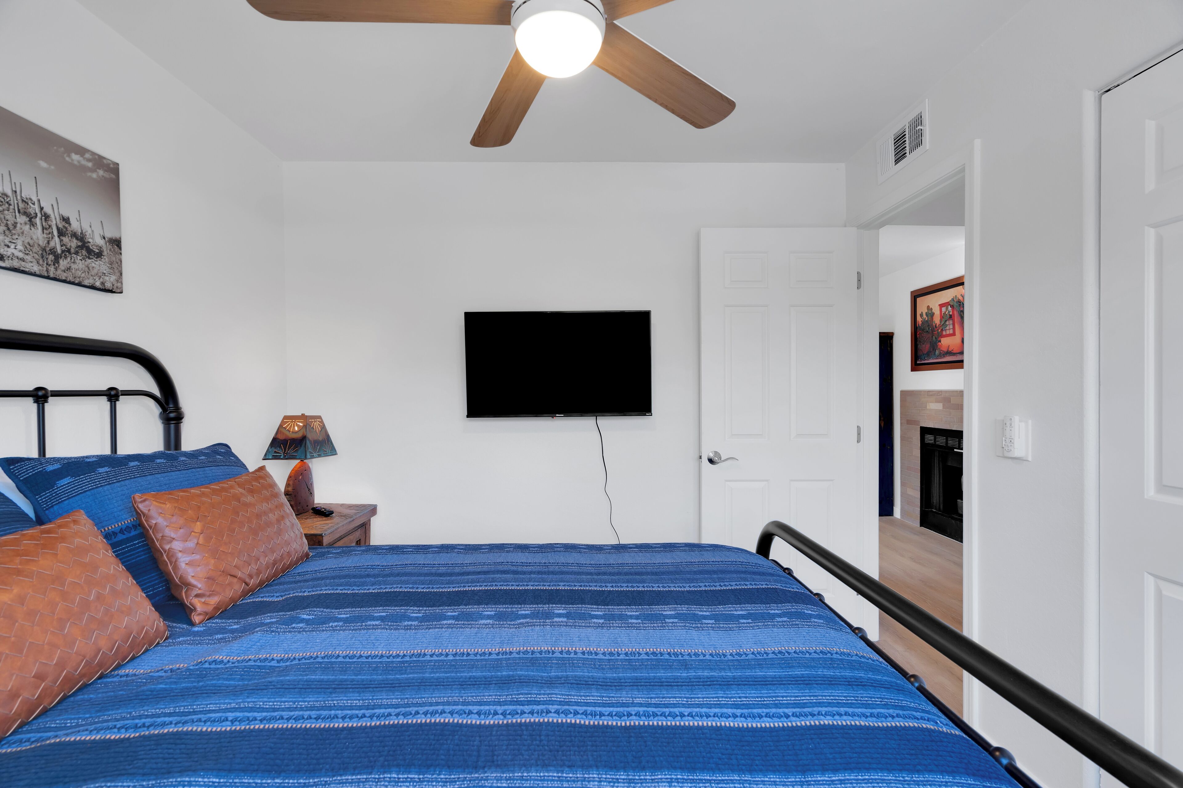 A bedroom with a bed, a ceiling fan, a TV mounted on the wall, and a door leading to another room.
