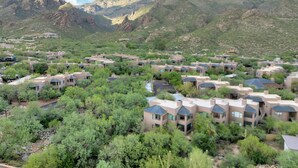 A residential area with multiple houses, surrounded by greenery and mountains in the background.