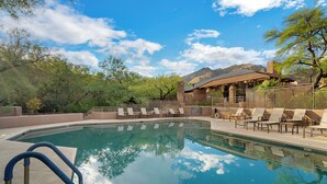 A pool with lounge chairs and a building with a mountain backdrop.