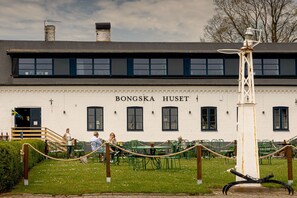 A building named BONGSKA HUSET with a white facade, multiple windows, and a green outdoor seating area with tables and chairs. - Bongska Huset (Abbekas)