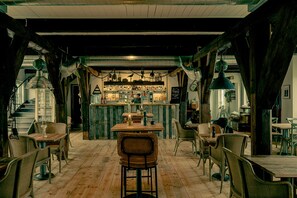 A rustic interior with wooden floors, metal-framed chairs, and a bar area with shelves of bottles. - Bongska Huset (Abbekas)