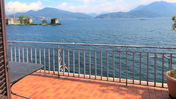 Un balcone con vista su un lago, un'isola distante con rovine e montagne sullo sfondo.
