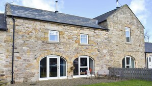 A stone building with a sloped roof, two arched windows, and a small porch area with outdoor seating.