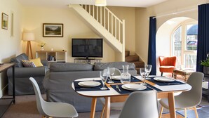 A modern living room with a dining area, a staircase, and a television.