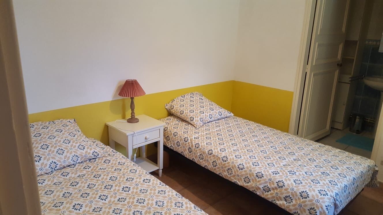 A small room with two beds, a nightstand, and a lamp.