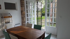 A dining area with a wooden table and chairs, a metal rack with dishes, and a view of a garden through a glass door.