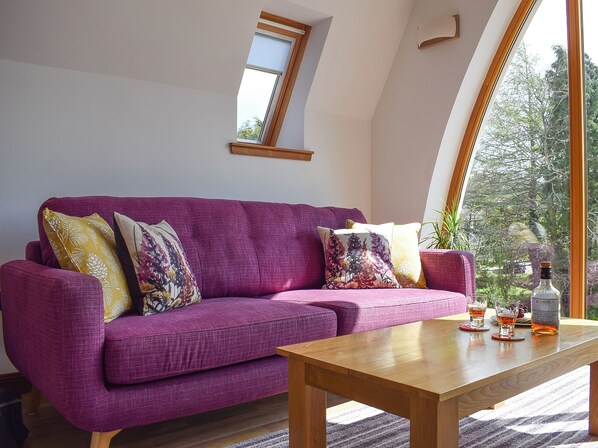 A purple sofa with patterned cushions, a wooden coffee table, and a bottle of liquor.