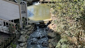 Een kleine waterval die over stenen in een vijver stroomt, omgeven door weelderige begroeiing en een houten terras.