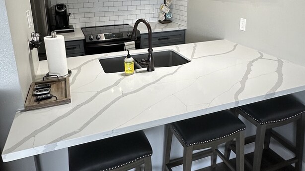Een keuken met grijze kastjes, een wit marmeren eiland en een roestvrijstalen magnetron.