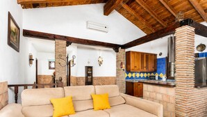 A living room with a beige sofa, a kitchen with a brick oven, wooden beams, and a tiled backsplash. - Villa Benizan Private Pool, Sea Views, A/C, WiFi (Torrox)