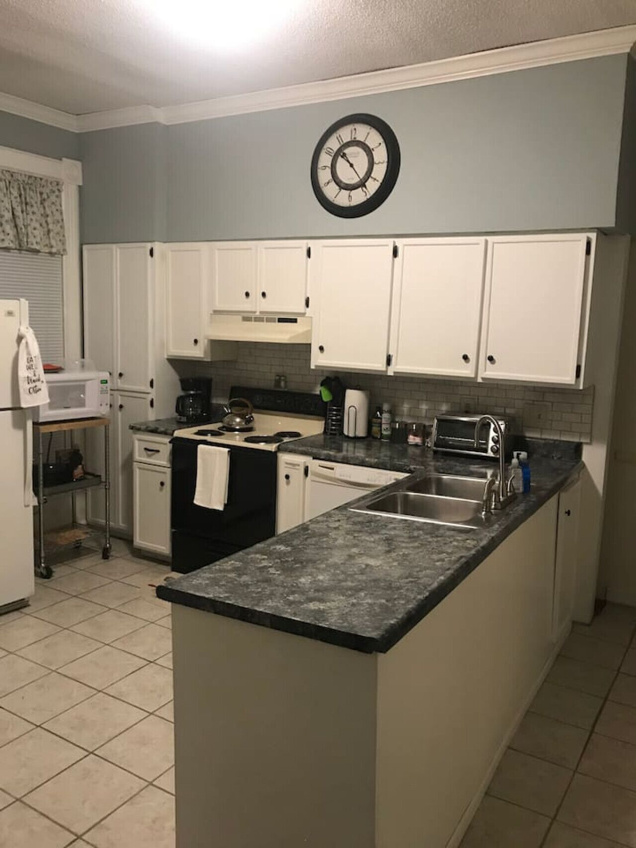 A kitchen with white cabinets, a granite countertop, a microwave, a stove, and a sink.