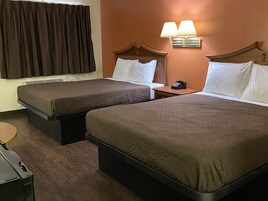 Quarto de hotel com duas camas, uma mesa de cabeceira com telefone e uma luminária na parede.
