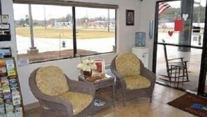 A room with two armchairs, a small table with a vase, a window with a view of a parking lot, and a refrigerator.