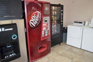 Máquina de refrigerantes Dr Pepper e máquina de café numa divisão com máquina de lavar roupa.