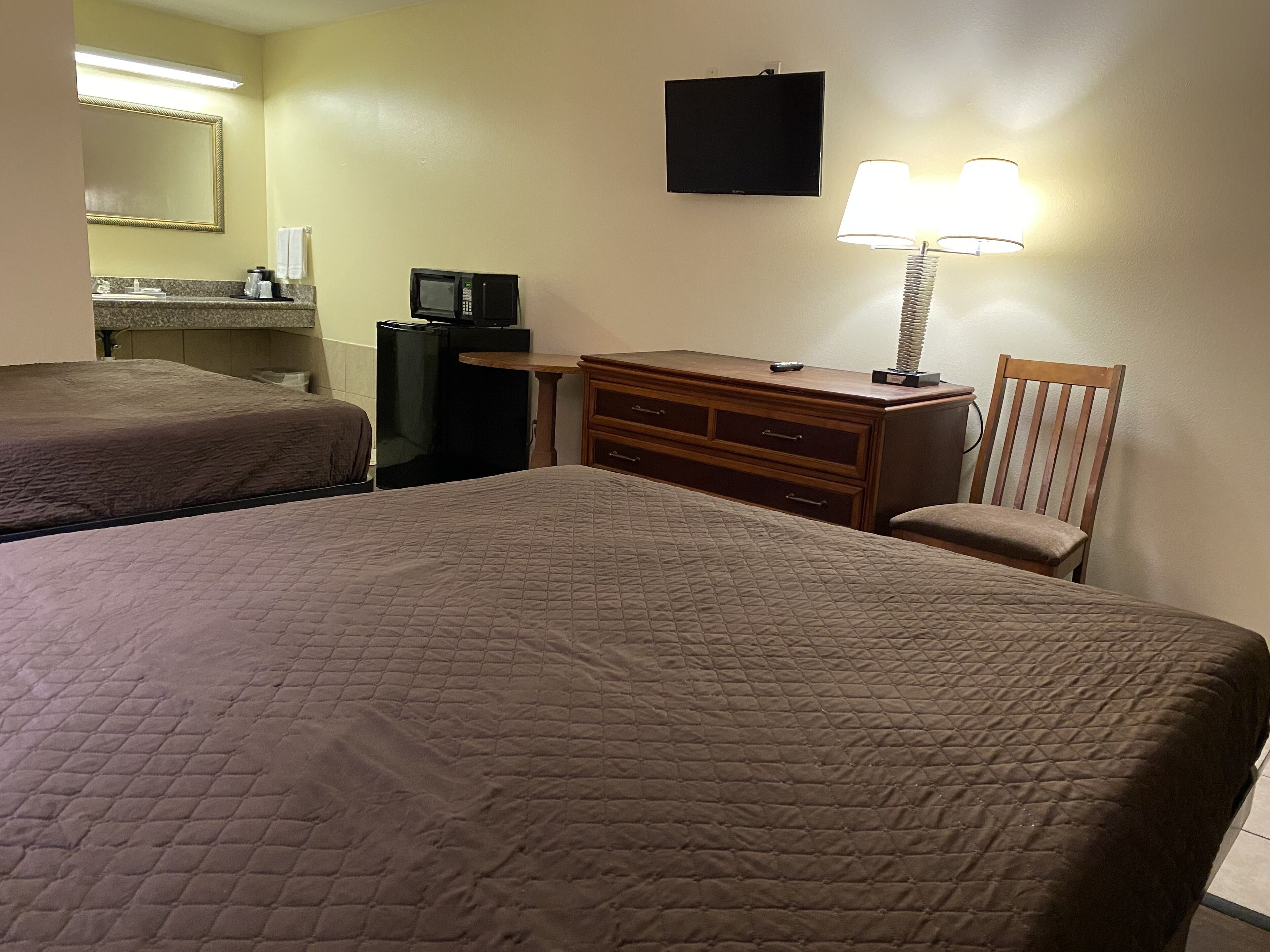 A hotel room with two beds, a desk, a chair, a dresser, a television, and a lamp.