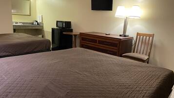 A hotel room with two beds, a desk, a chair, a dresser, a television, and a lamp.
